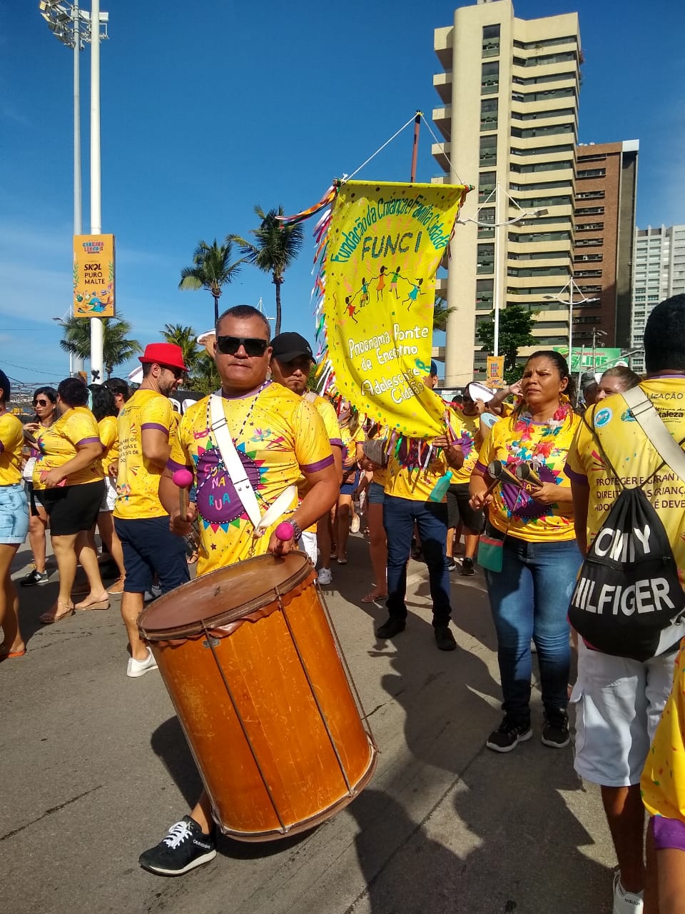 pessoas com blusa igual com nome do bloco desfilando em rua e tocando instrumentos de percussão